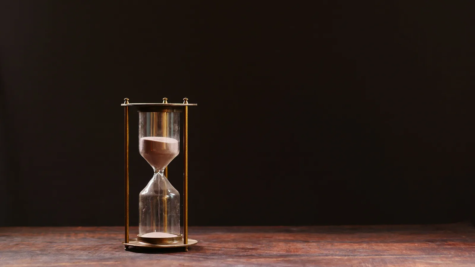 Hourglass with sand running against a dark background