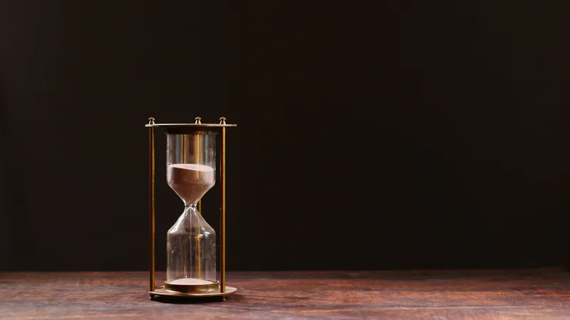 Hourglass with sand running against a dark background